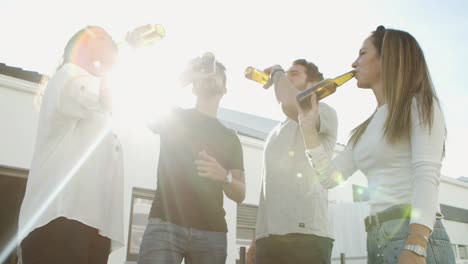 relaxed friends clinking beer bottles and dancing outdoors