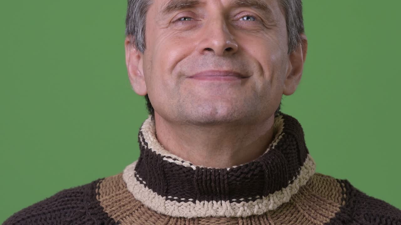 hombre guapo maduro con suéter de cuello alto contra un fondo verde