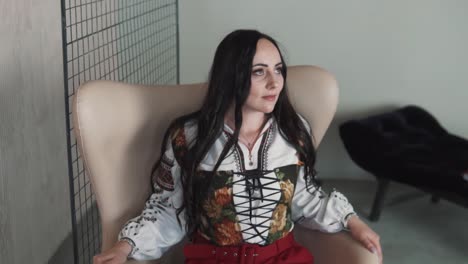 una encantadora mujer joven se sienta en una silla vestida con una elegante camisa y corsé ucraniano bordado auténtico
