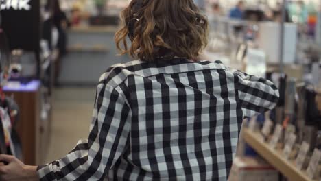 Rare-view-of-cute-caucasian-pretty-young-woman-with-short-curly-hair-and-in-headphones-dancing-and-listening-music-in-the-middle-of-the-supermarket-with-household-stuff