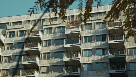 modern apartment building with balconies, some featuring plants, and branches framing the scene