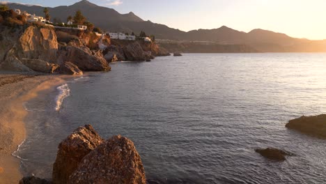 Impresionante-Puesta-De-Sol-En-Una-Pequeña-Playa-De-Arena-Con-Villas-En-Acantilados-Y-Océano