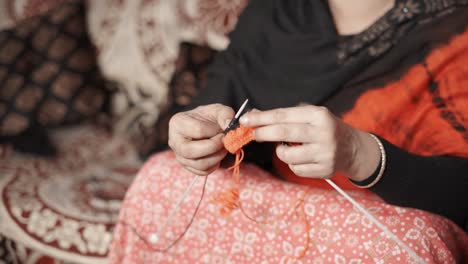 woman's hands knits with craft needles and red and black thread