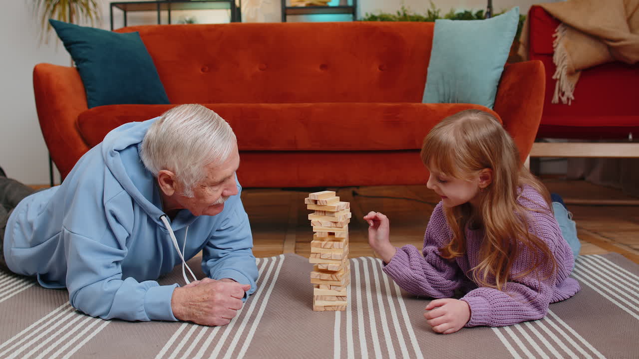 Excited little child girl granddaughter playing building block game with smiling grandfather at home