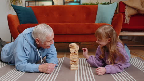 excited little child girl granddaughter playing building block game with smiling grandfather at home