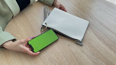 una mujer de 4k saca un teléfono con pantalla verde de su bolso.