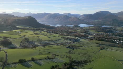 busy road cutting across fields towards town of keswick with distant lake and misty mountains in the background