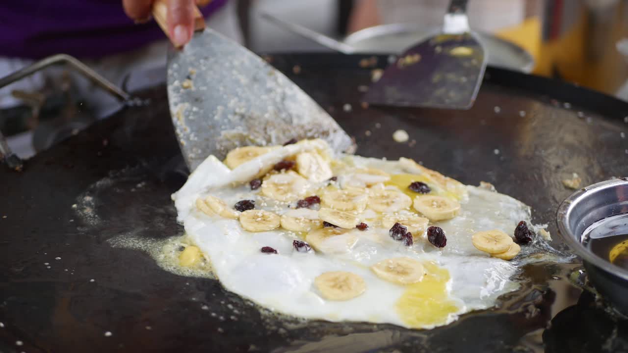 Eggs with banana and raisins fried in a pan at the night market. Sweet street food. 4k