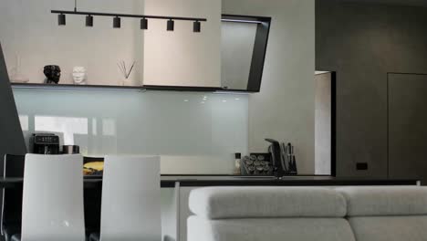 modern kitchen facade at home with white interior, refrigerator, gas stove appliance, cooking hood, built in oven, sink, water tap, kitchenware supplies on shelves and plants on cupboard furniture