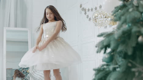 beautiful girl spinning near christmas tree in white dress.