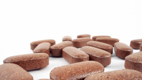 close-up of brown, textured herbal supplement pills on a white background