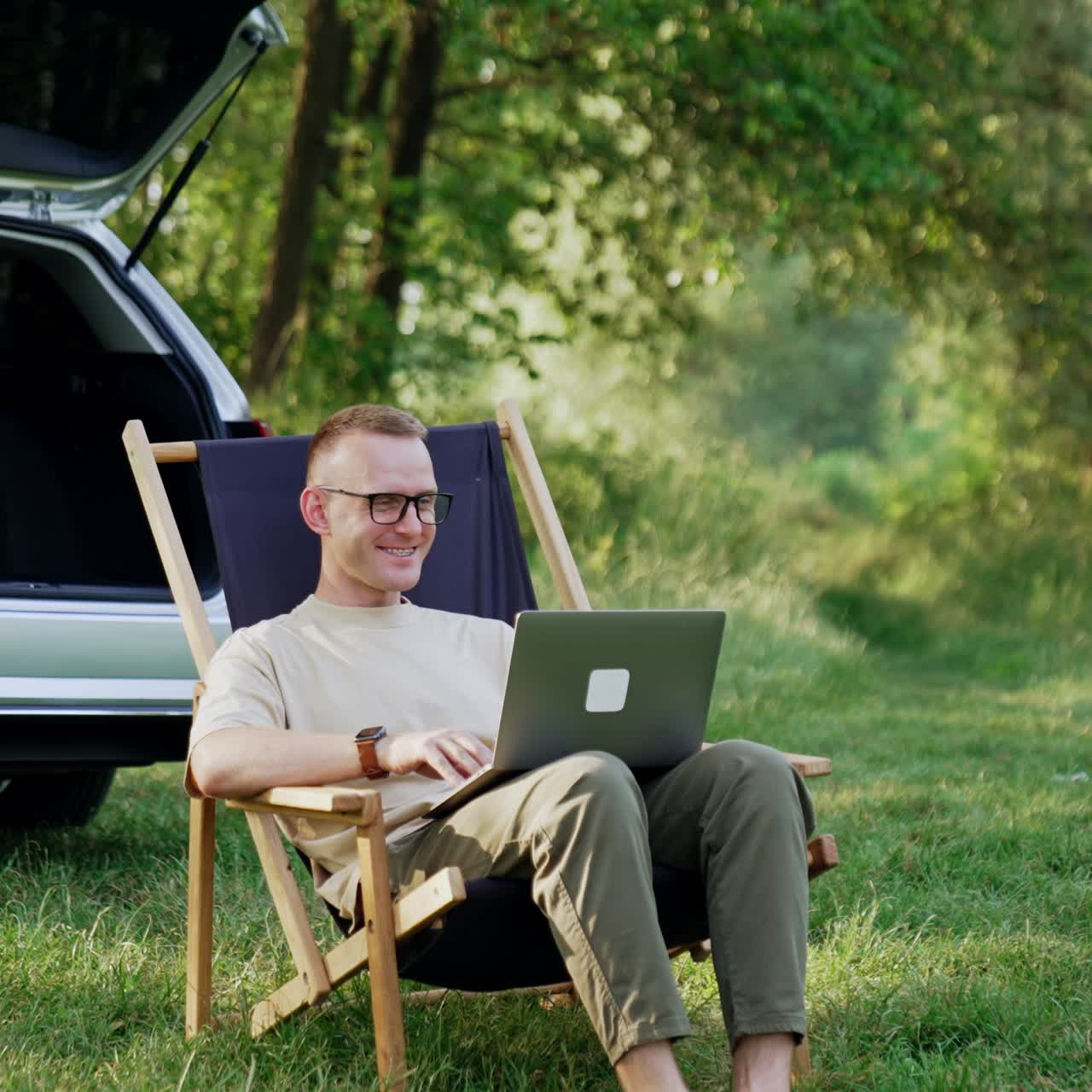 Smiling male freelancer work remote on laptop. Man in glasses is happy to work in nature