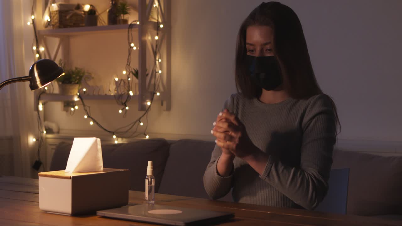 Woman wearing mask cleaning laptop at home at night