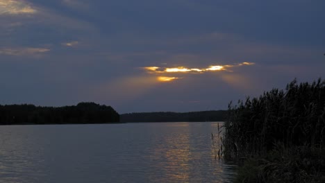 Puesta-De-Sol-Dorada-Escondida-A-Través-De-Las-Nubes-Sobre-El-Lago-Tranquilo-En-El-Parque-Paisajístico-Wdzydze-En-Polonia---Toma-Amplia