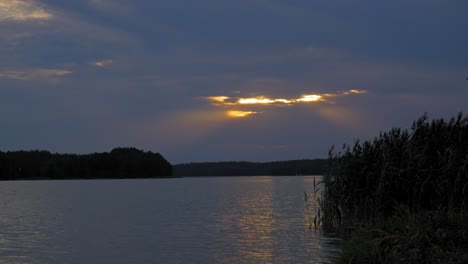 puesta de sol dorada escondida a través de las nubes sobre el lago tranquilo en el parque paisajístico wdzydze en polonia - toma amplia