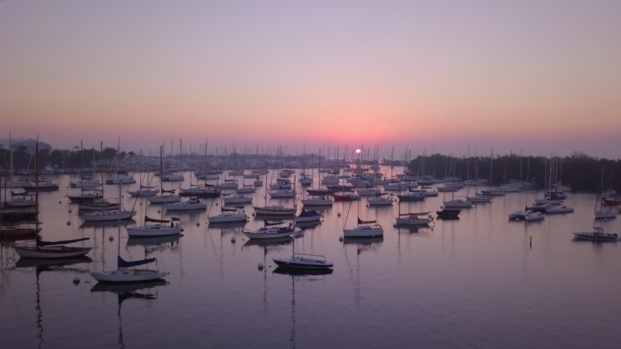Aerial fly up to reveal boat filled harbor and sunrise