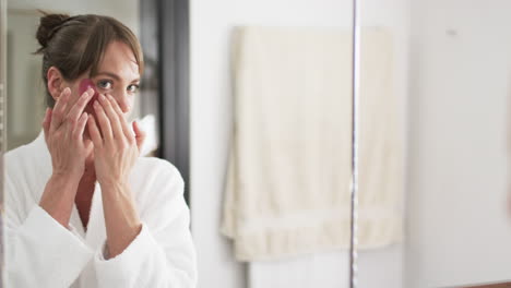 Middle-aged-Caucasian-woman-applies-skincare-in-a-bathroom,-with-copy-space