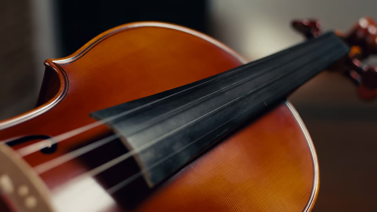 Primo Piano di un Corpo di Violino Lucidato in Calda Luce da Studio, Liutaio che Ispeziona Ponticello e Tastiera, Ricca Vernice