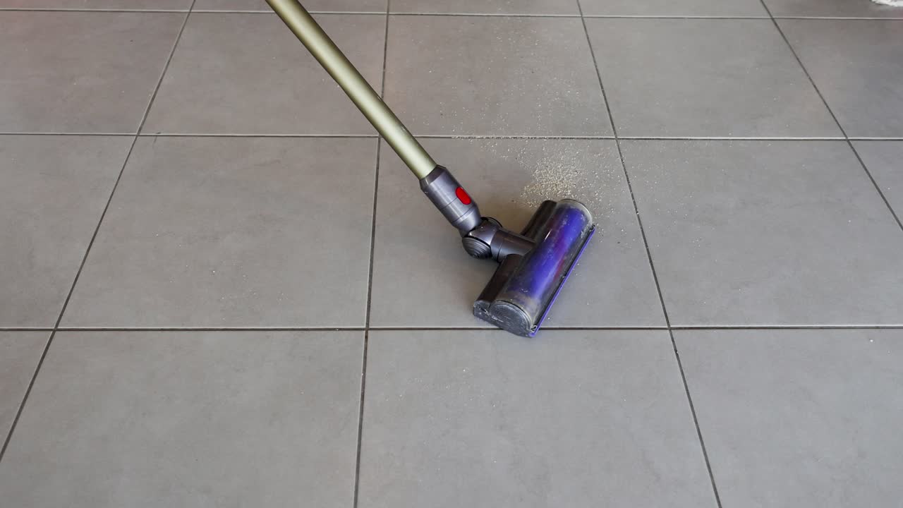 A vacuum cleaner removes crumbs from kitchen tiles. Bright lighting highlights the cleaning process and tile texture