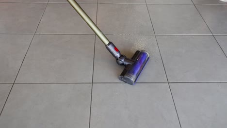 a vacuum cleaner removes crumbs from kitchen tiles. bright lighting highlights the cleaning process and tile texture