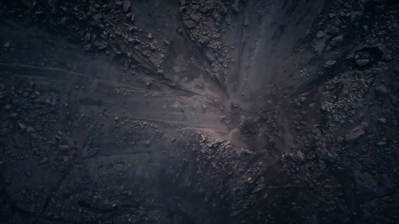 Zoom della camera che mostra i canali erosi centrali su un pendio brullo, rivelando rocce e anello di cicatrice