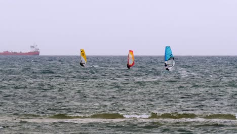 orange and blue windsurfing riding the waves in a choppy sea and big boat on background