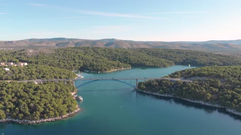 Aerial view of highway bridge in a natural wild environment mountain and sea, traffic car and yacht parking on the river.