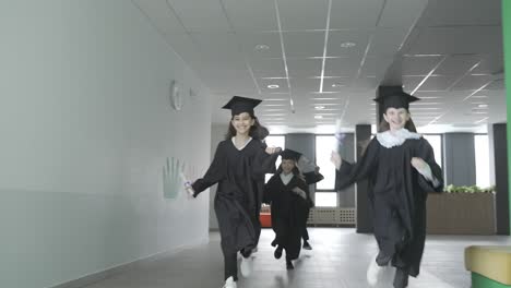 grupo de felices estudiantes de preescolar multirraciales con birrete y bata. están corriendo y sosteniendo diplomas.