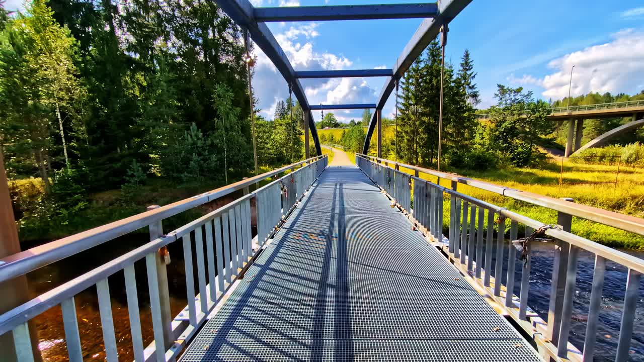 Metal footbridge over river in forested area with clear blue sky in summer