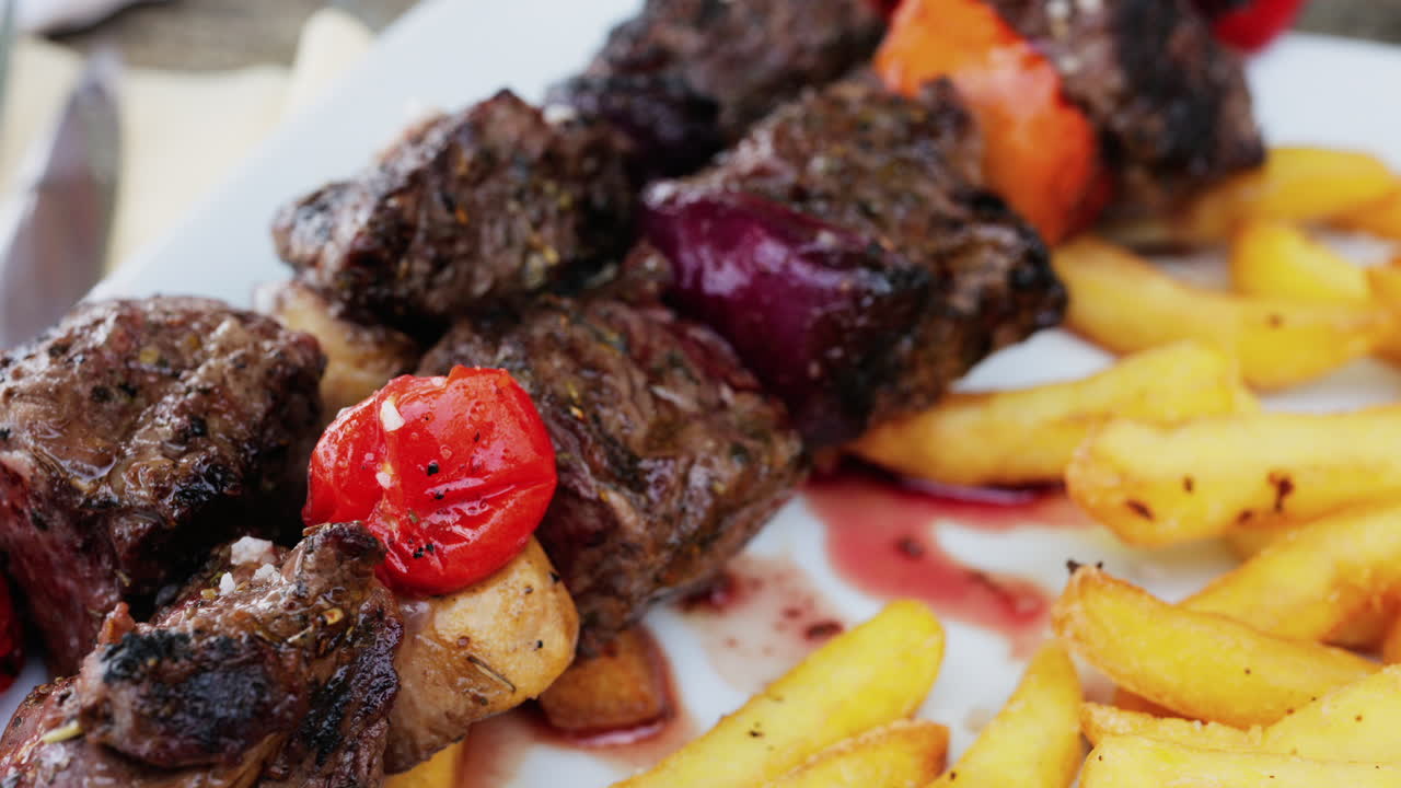 Primo piano di spiedini di maiale grigliato con pomodori e patatine fritte in un piatto bianco al ristorante