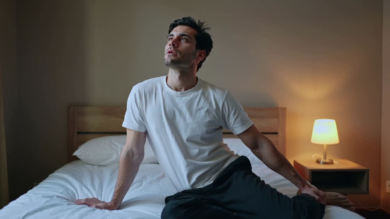 Video verticale: Uomo adulto che sposta il busto e solleva il mento, tenendosi al letto per allungare il collo.