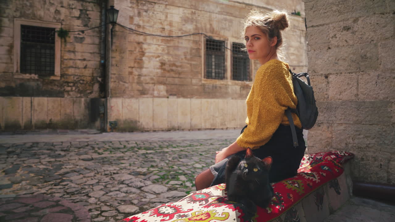 Cinemagraph 4K UHD di una giovane donna bruna seduta accanto a un gatto nero nella famosa città vecchia di Cattaro in Montenegro