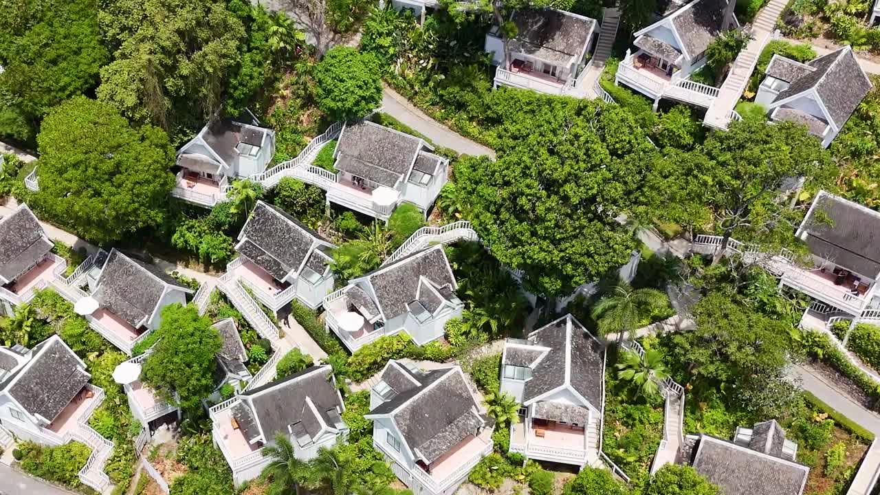 드론 영상은 태국 푸켓의 울창하고 열대적인 리조트를 포착합니다. 위에서 빌라, 수영장, 그리고 초록색을 보여줍니다.