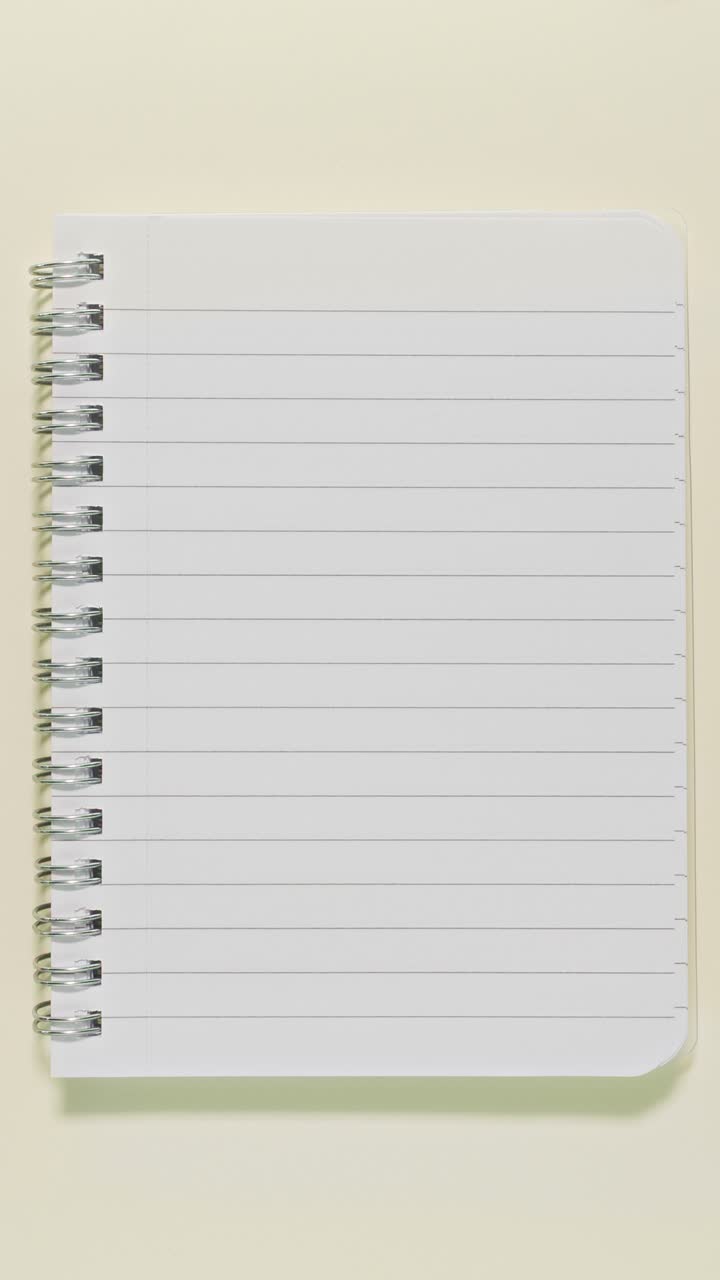 Portrait stop-motion loop of a lined spiral notebook used as copy space, surrounded by school and office items