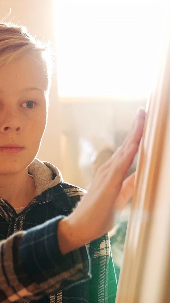 Young child with focused expression is painting on canvas in a sunlit room, showcasing creativity and artistic exploration in a warm atmosphere