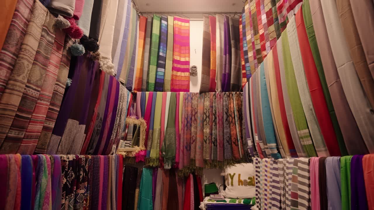 Rows of colorful Moroccan scarves and shawls are neatly arranged inside a traditional market stall