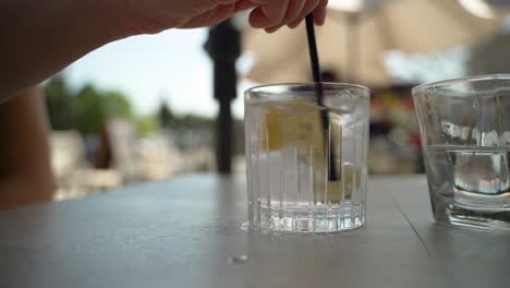 hand mixes glass of water with lemon and lime in it on a patio table