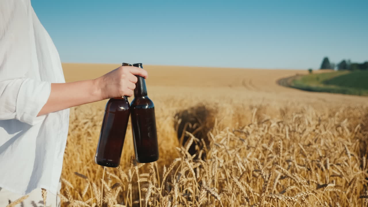 женщина несет две бутылки пива по полю спелой пшеницы