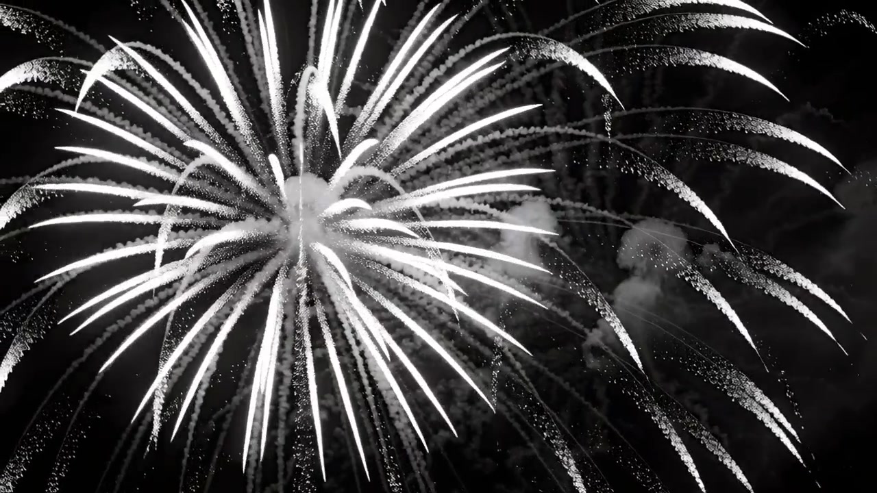 Esplosione di un grande fuoco d'artificio che lancia lunghe scie di scintille nel cielo notturno, creando pennacchi di fumo.