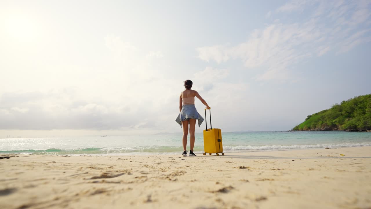 4к азиатская женщина тащит чемодан и гуляет по тропическому пляжу на летнем закате.