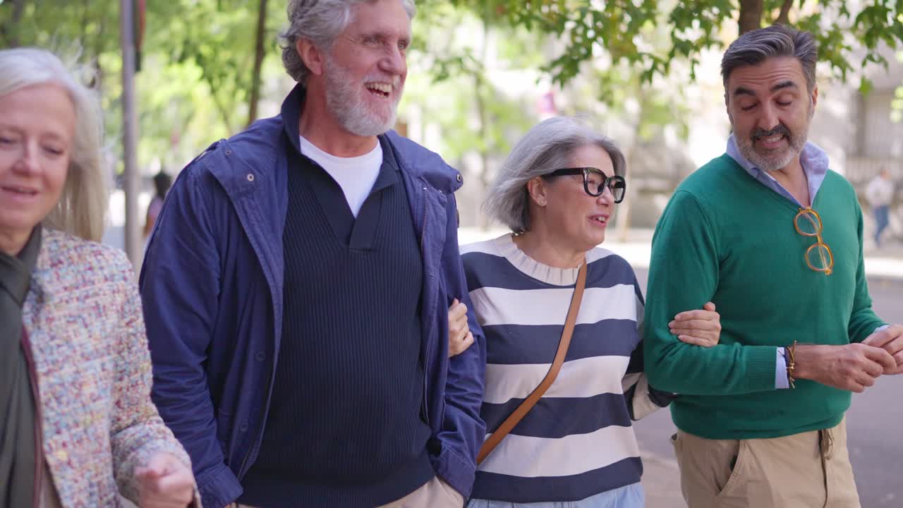 Grupo de amigos idosos felizes caminhando e conversando de braços dados na cidade