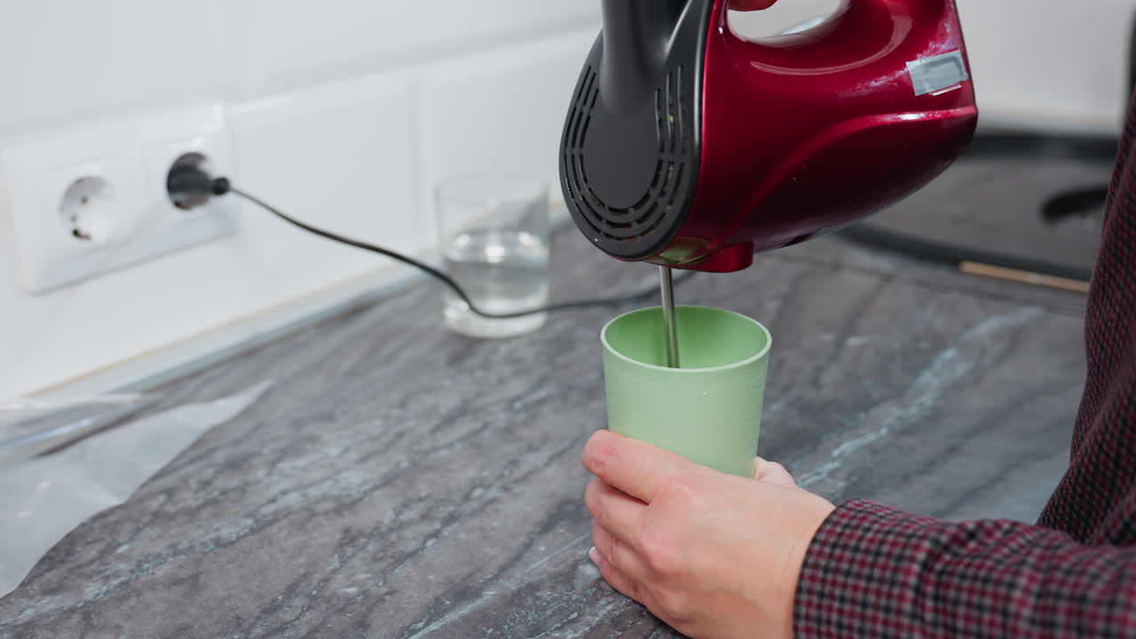 녹색 컵에 뜨거운 물을 는 누군가의 가까운 위에, 벽 소켓과 유리 컵에 연결된 전선이 테이블에 놓여있는 동안, 물에서 증기가 아지면서, 부 환경