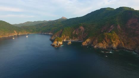 drone video sliding along the rough terrain at carrizal anchorage by manzanillo mexico at sunset overlooking sailboats anchored in the bay