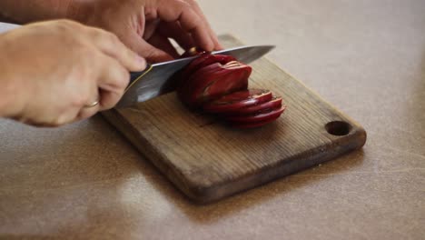 cortar un tomate rojo oscuro en rodajas sobre una mesa de madera