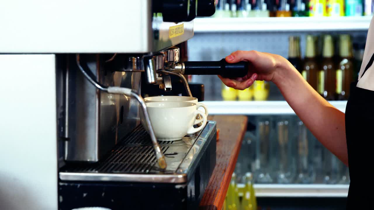 Waitress making cup of coffee at counter in kitchen