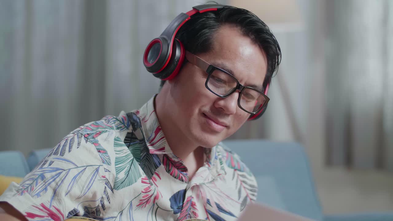 집에서 기타를 연주하는 동안 노트북과 종이를 보는 아시아 남자 작곡가의 클로즈업