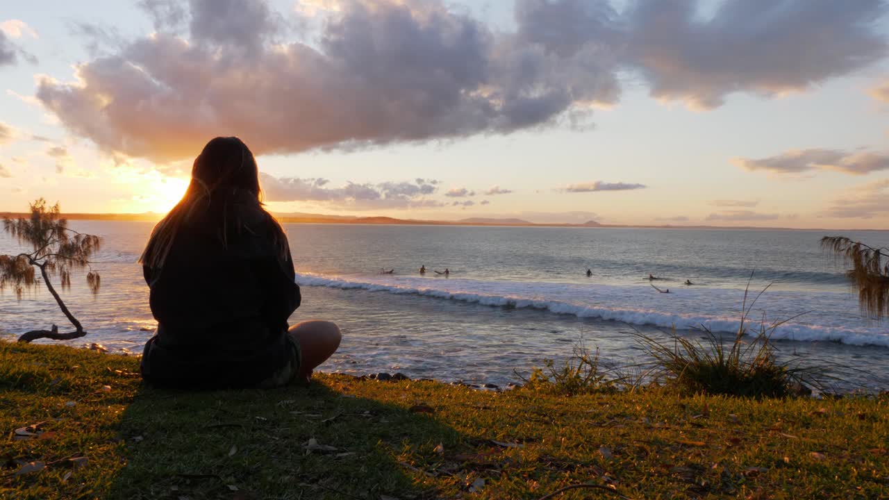 vista detrás de una mujer sentada en la costa y viendo a los surfistas en laguna bay con fondo iluminado por el sol