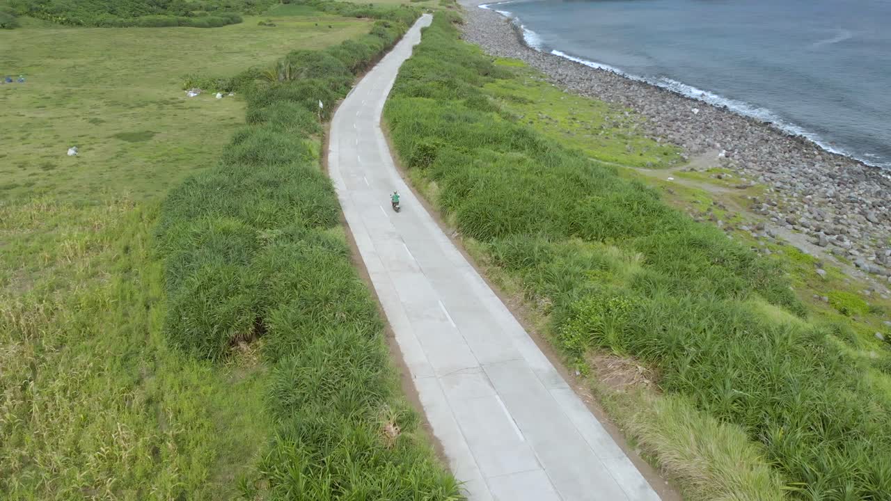 A drone follow clip of a man riding a scooter on the hills of Batanes