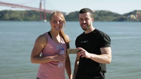 smiling sportsmen standing on riverside with smartphone.