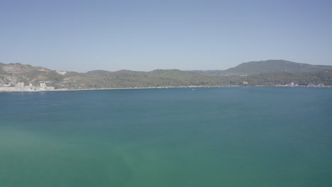 Toma-Aérea-De-Pequeños-Barcos-De-Pesca-Que-Salen-De-Un-Muelle-En-El-Mar-Atlántico-Azul-Profundo-Con-Agua-Clara-Y-Cielo-Azul-En-Un-Día-Soleado